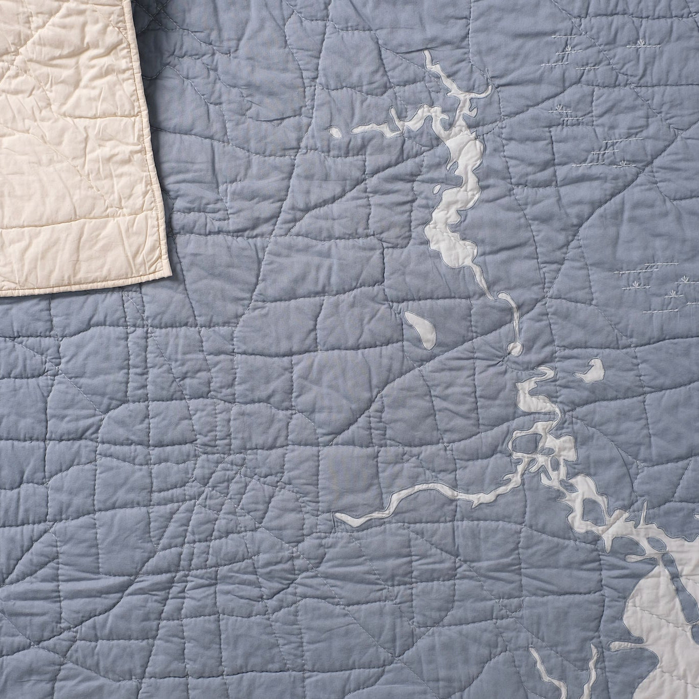 close up of a hand quilted steel blue and light blue Houston quilt with one corner folder down to see the ivory back