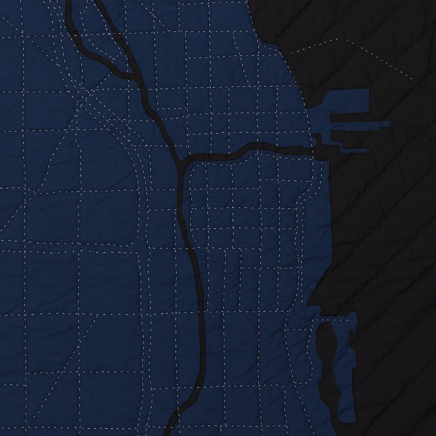 Detail of heirloom quilt, a hand-stitched map of the Chicago River and Lake Michigan with dark blue land and black water.
