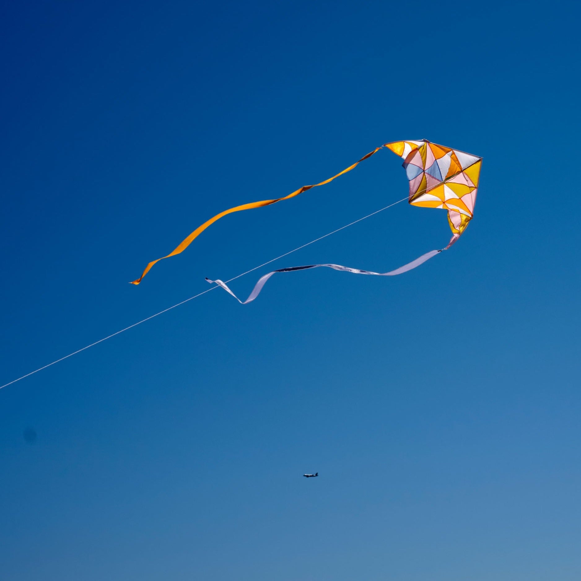Yellow patchwork delta kite flying through the blue sky with two tails_Haptic Lab