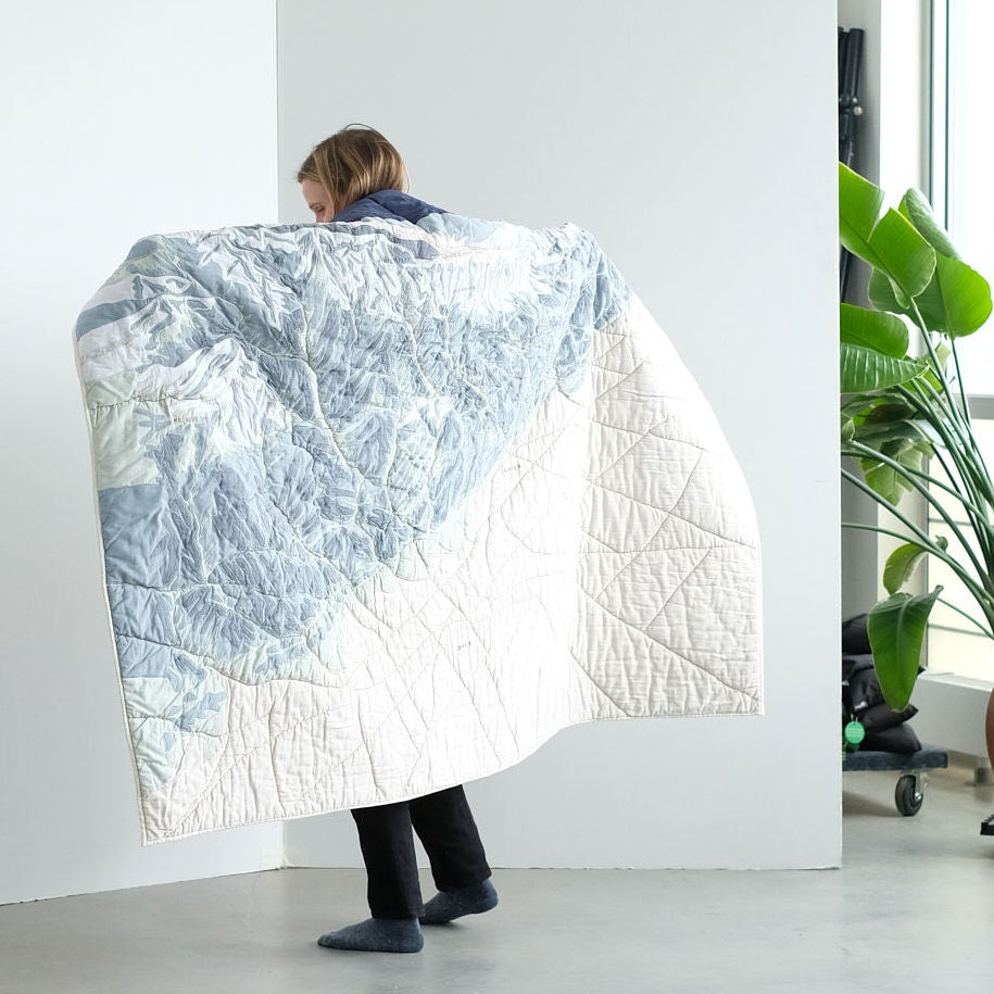 Person holding a large quilt with the Front Range appliqued on it in a modern setting. 