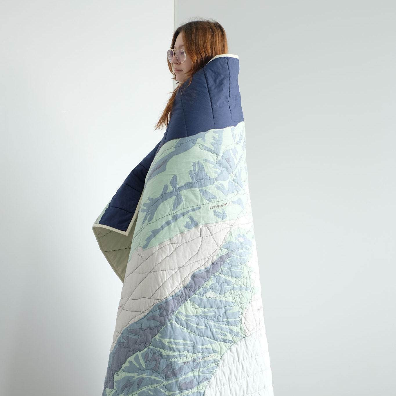 Person wrapped in a large quilt with Los Angeles landscape quilt against a white background