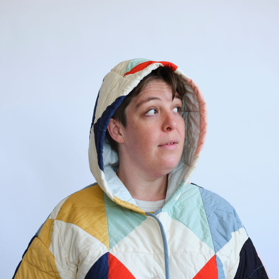 Hood up on the Harlequin Quilt Coat. Ivory quilt coat with multicolored diamond patchwork. Quilt Coat by Haptic Lab