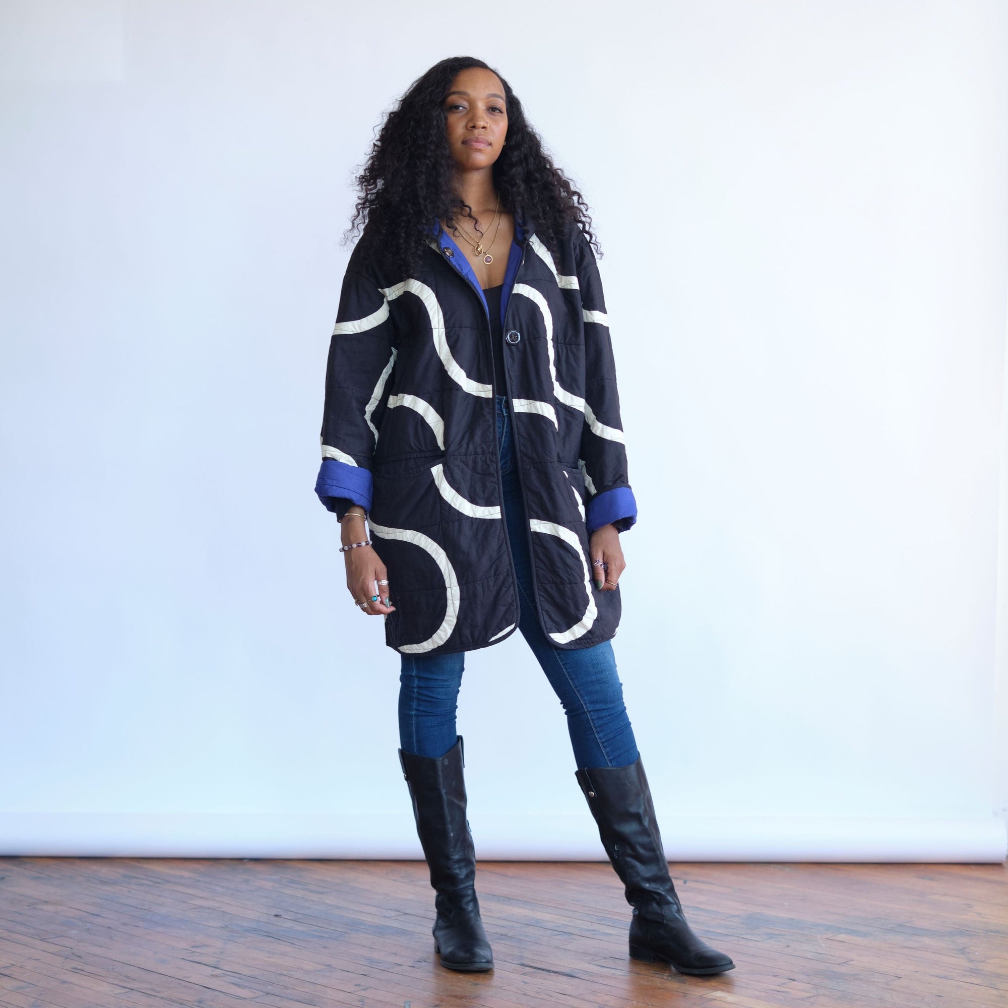 Snake Path Quilt Coat by Haptic Lab. Black quilt coat with white patchwork snake design. Sleeves rolled up to show blue interior of the coat. 