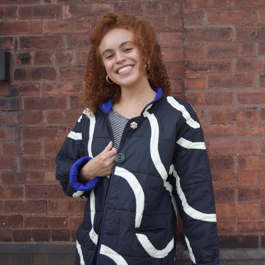 Woman wearing a patterned jacket standing against a brick wall