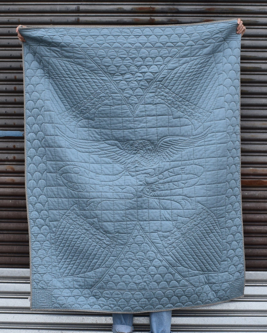 Blue American quilt with geometric pattern held up against a metallic background