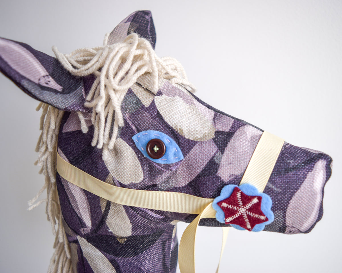 Purple Oberon hobby horse close-up, showing a blue felt eye surround and burgundy star on a blue felt rosette.