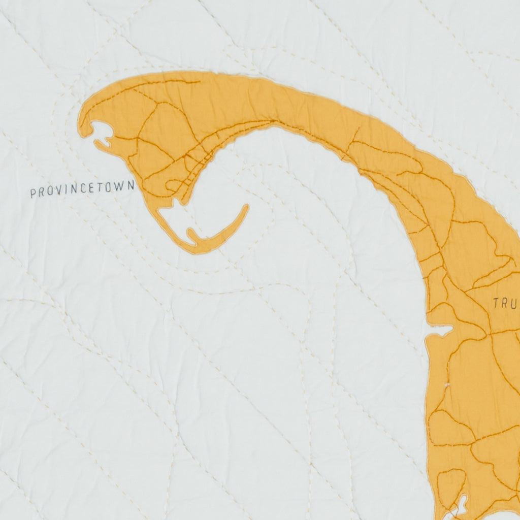 Detail of heirloom quilt map of Cape Cod's Provincetown with yellow gold land and pale blue water. Place names stitched in dark gray.