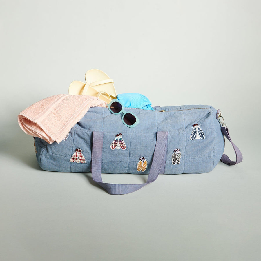 Cicada Duffle bag with towel, yellow flip flops, sunglasses coming out of bag.
