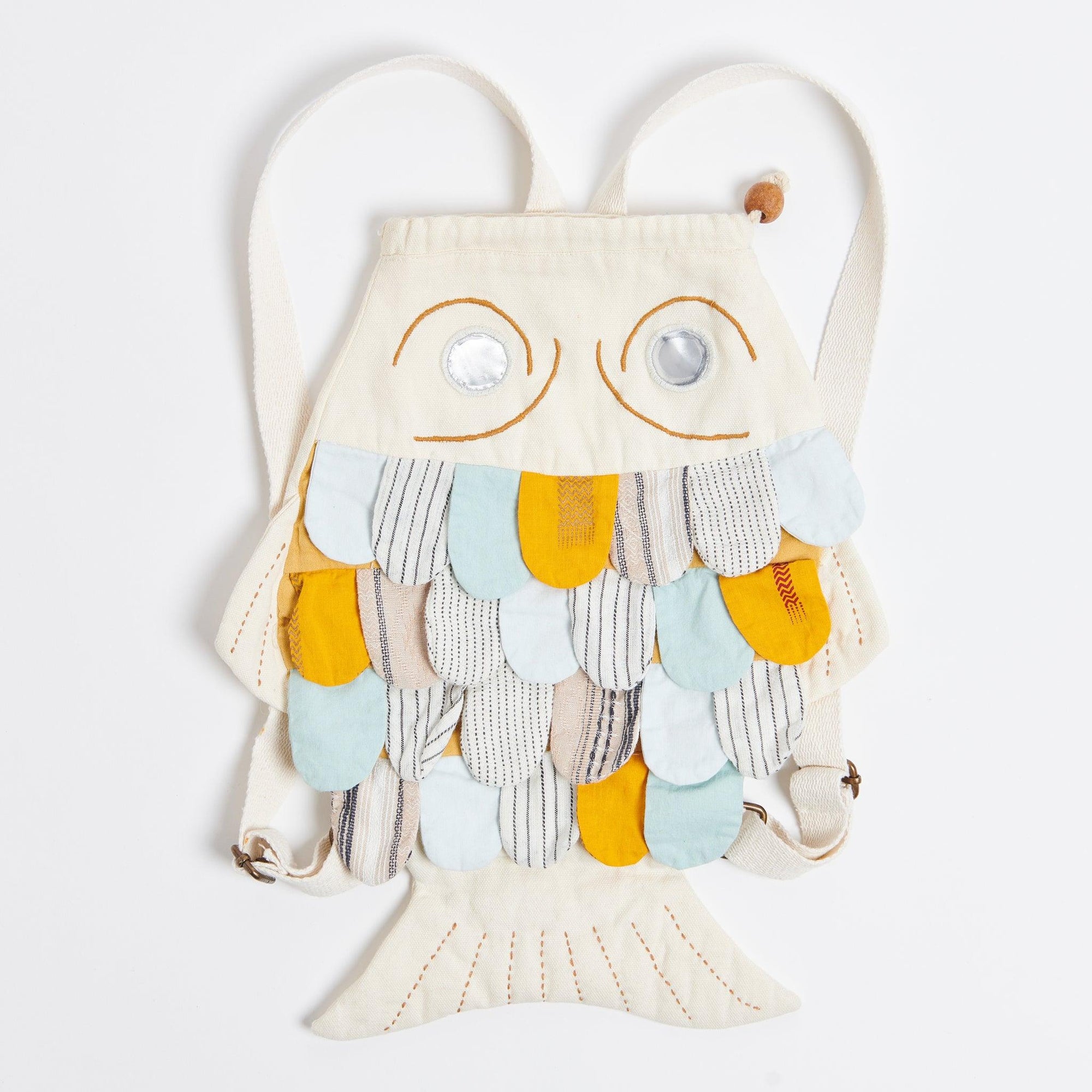 White fish shaped backpack on a white background. Fish has mettalic eyes and scales made out of patchwork fabrics