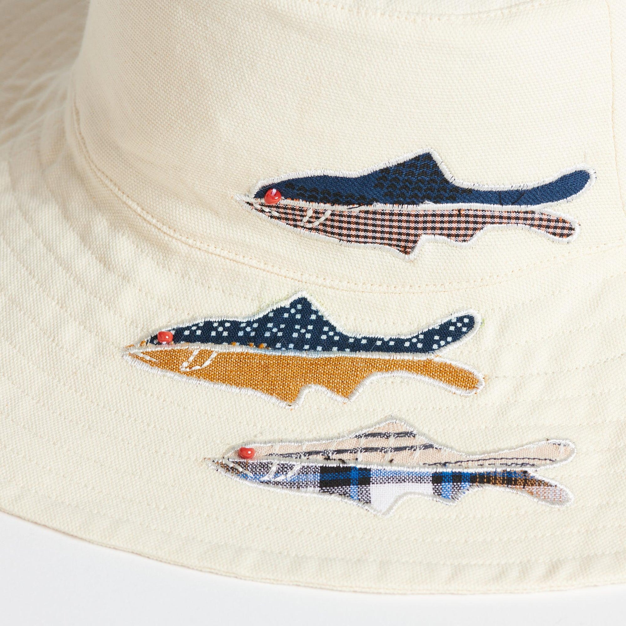 Close up of three appliqued fish on the white sun hat. Each Fish is made up of two deadstock cotton fabrics, split horizontally. 