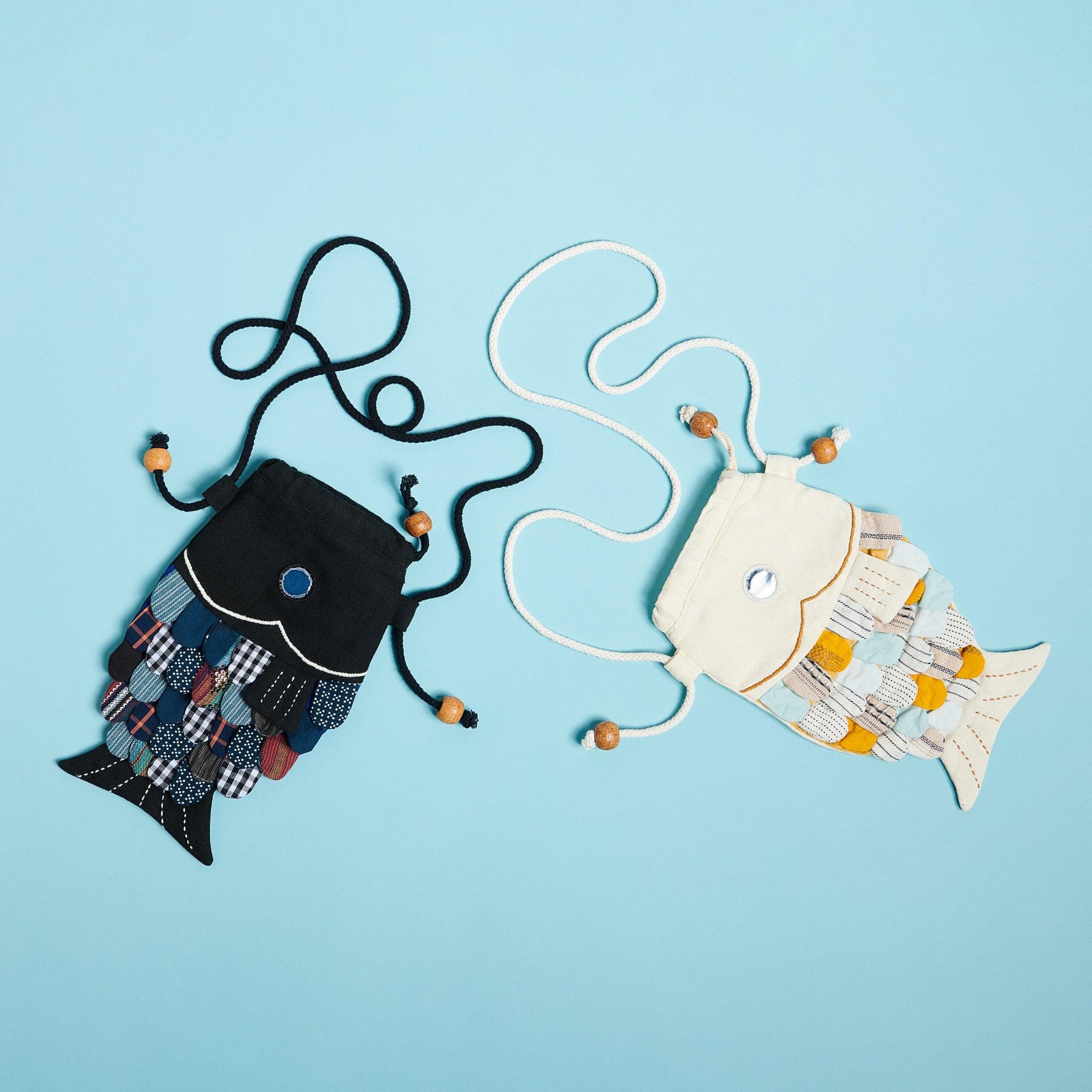 Black patchwork fish purse and white patchwork  fish purse on blue background. p