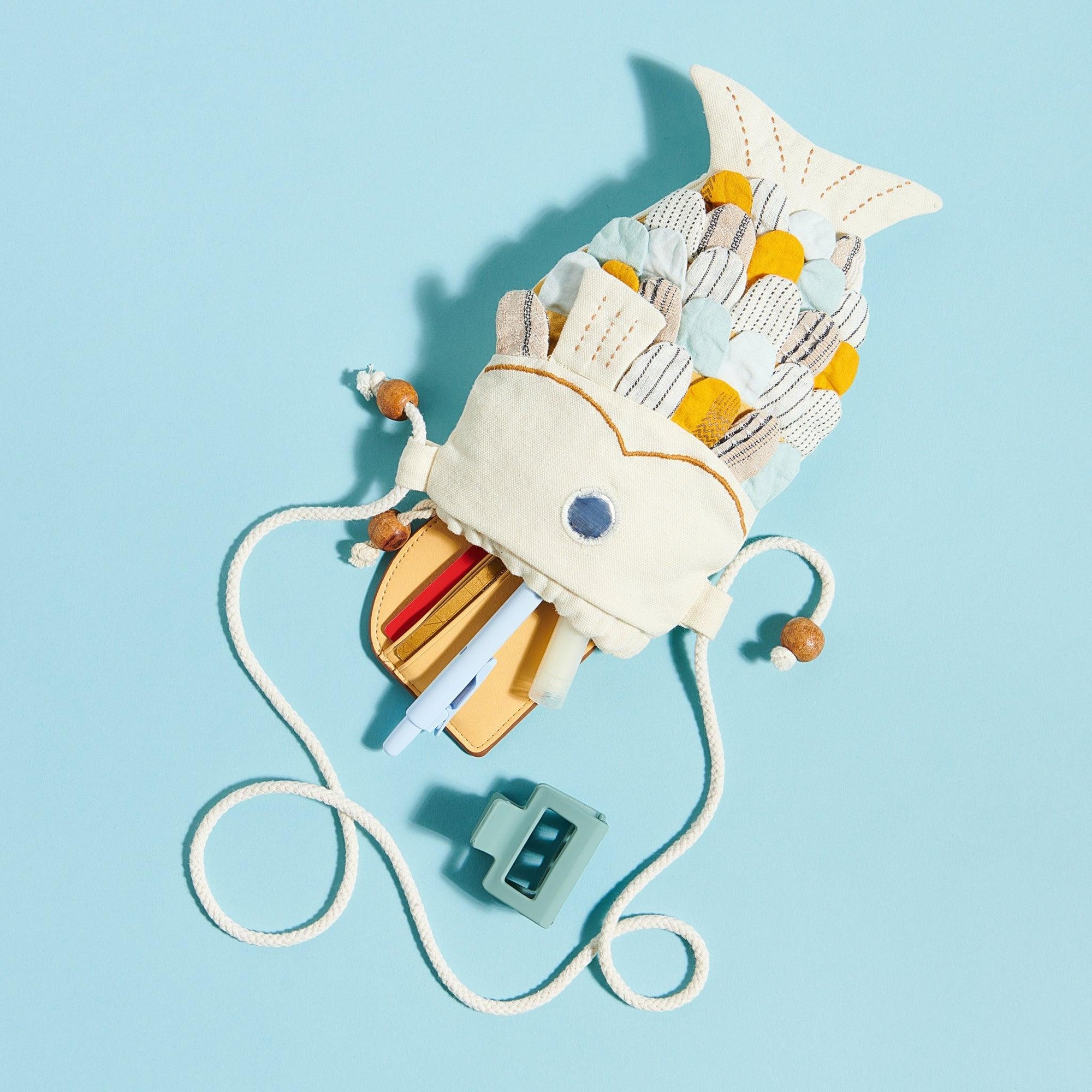 White fish purse on blue background with pens and wallet coming out of the mouth of the fish. 