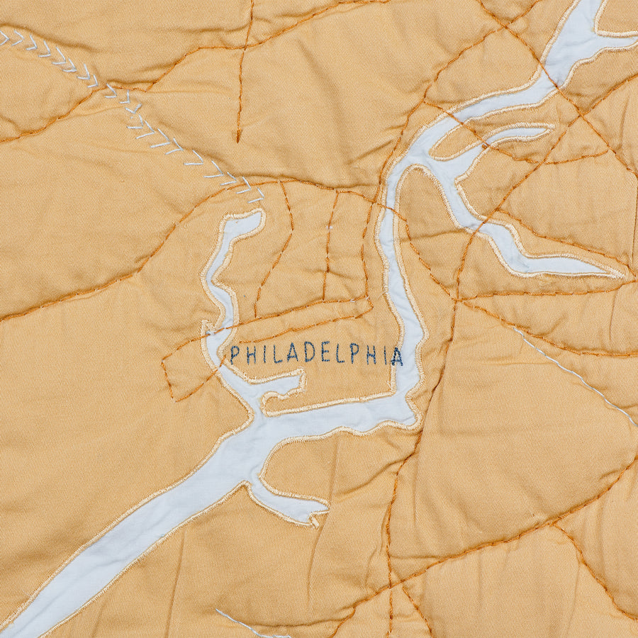 Detail shot of Philadelphia on the Jersey Shore coastal quilt. Land is gold, the river is pale blue.