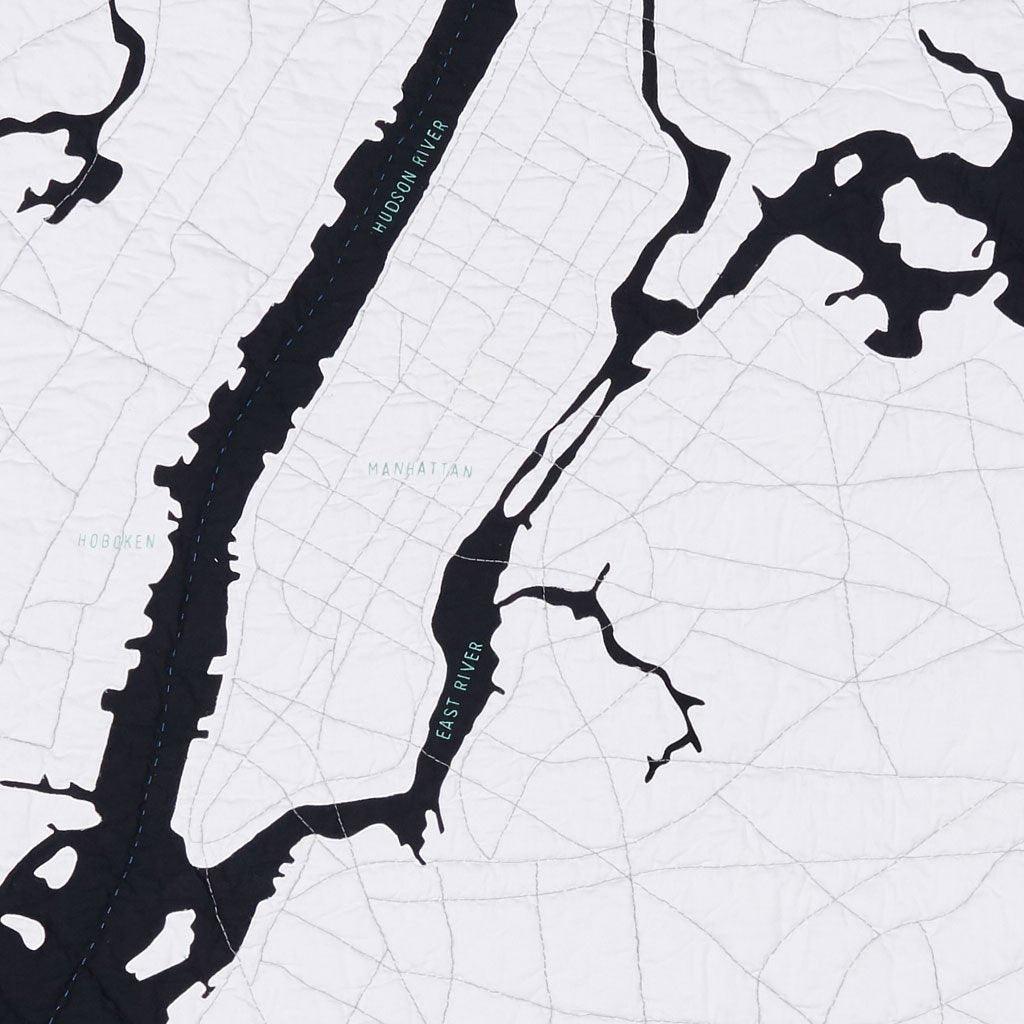 Detail of the New York City Quilt by Haptic Lab showing Manhattan Island in white cotton with city streets stitched, surrounded by waterways in contrasting black cotton..