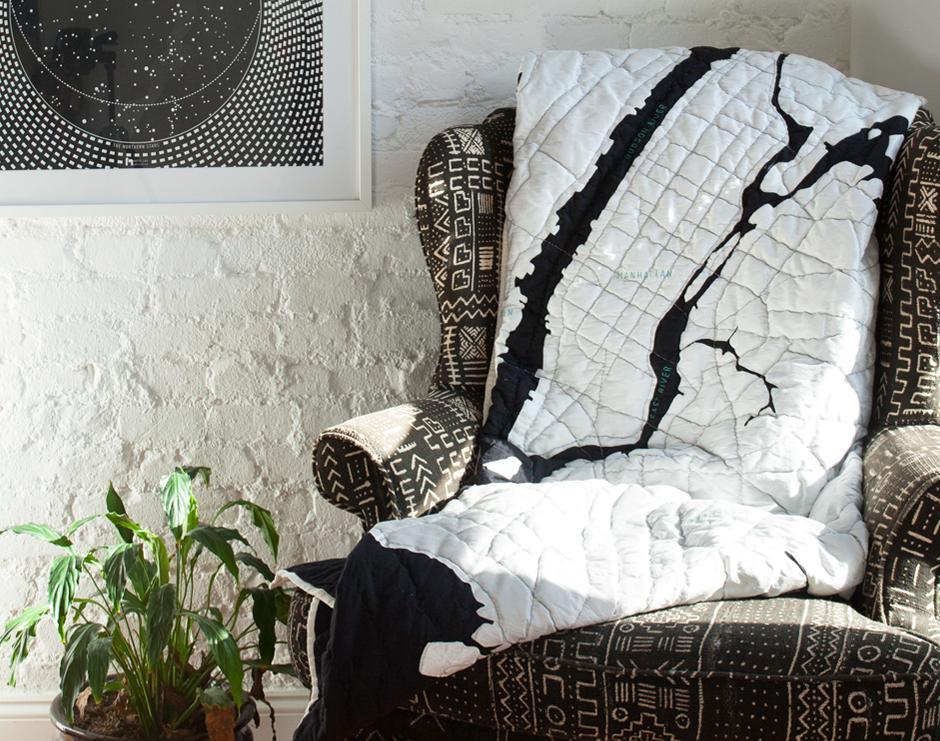 The New York Harbor Quilt Map by Haptic Lab draped over an armchair in the sun, showing the city streets of the map quilted on black and white cotton.
